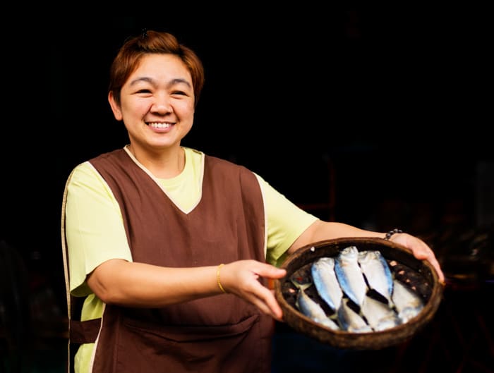 Una mujer posando con una canasta de pescado contra el fondo negro
