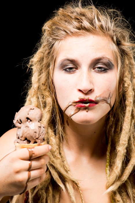 Una chica rubia con helado de chocolate en la cara contra un fondo negro - accesorios fotográficos