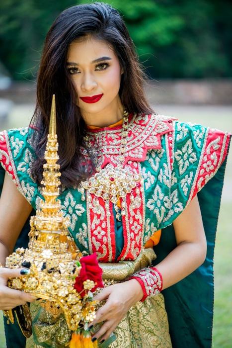 Una hermosa modelo femenina con traje clásico tailandés sosteniendo accesorios fotográficos para un impacto adicional