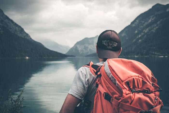 Foto de un chico con una mochila parado al lado de un lago