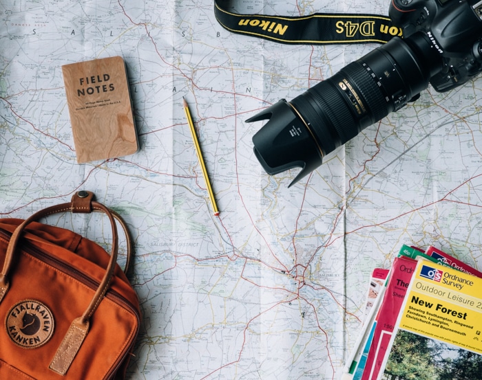 Foto de una cámara, un mapa, una mochila y un bloc de notas.