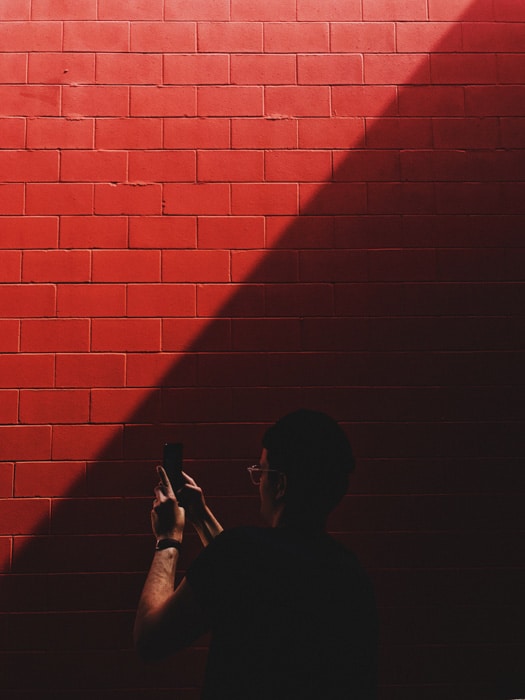 Un hombre tomando una foto con un teléfono inteligente de una pared de ladrillo rojo - procesamiento de película de empuje