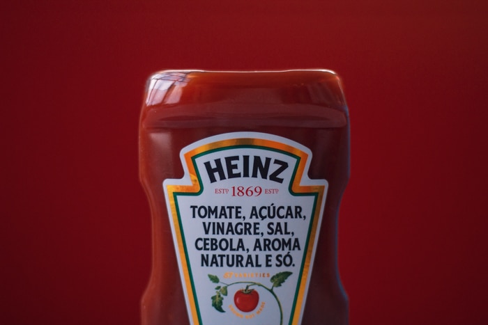 Cerca de la mitad de la botella de Heinz Ketchuo contra el fondo rojo oscuro coincidente