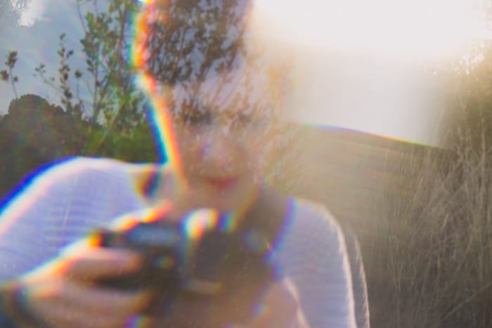 Una mujer con un top a rayas sosteniendo una cámara, superpuesta con un efecto fotográfico de prisma de ensueño