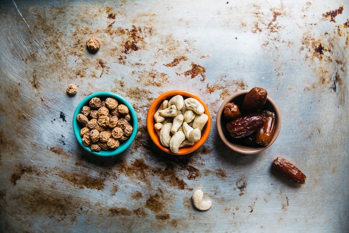Una fotografía cenital de tres pequeños tazones de nueces y frutos secos sobre una superficie metálica