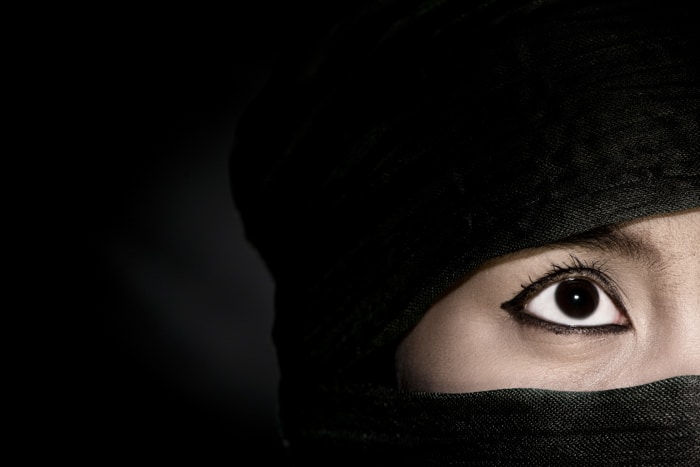 Un misterioso retrato de cerca de un modelo femenino en un pañuelo negro sobre fondo negro - errores de iluminación de fotografía