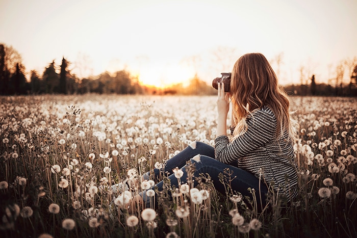 Chica en un campo tomando una foto del paisaje