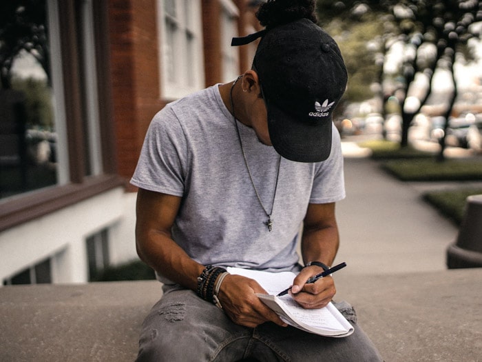 Un hombre con sombrero negro sentado en un muro de piedra escribiendo un formulario de autorización modelo para fotografía
