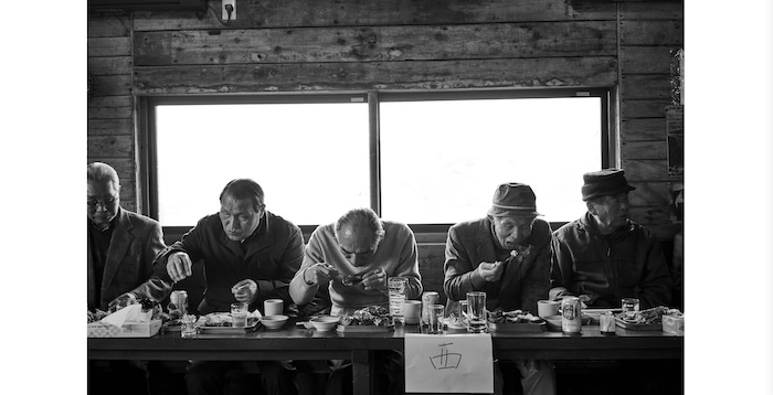 Fotografía en blanco y negro de un hombre mayor comiendo en una mesa por Gentl & Hyers