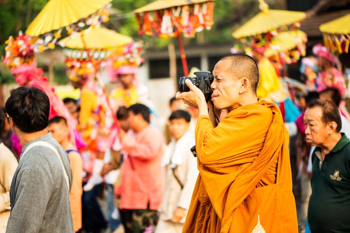 Un monje budista tomando fotos con una DSLR al aire libre entre multitudes: cómo iniciar un club de cámaras