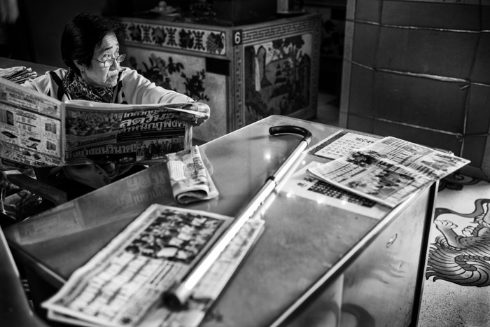 Retrato en blanco y negro de una mujer leyendo un periódico en una mesa