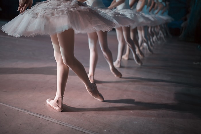 Las piernas de una fila de bailarines en tutú blanco bailan sincronizados en el escenario