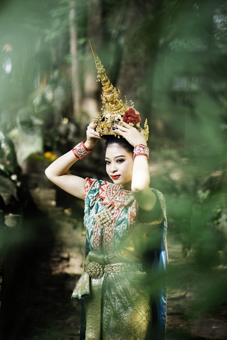 Una foto de una mujer tailandesa en traje tradicional enmarcada por un árbol en primer plano.