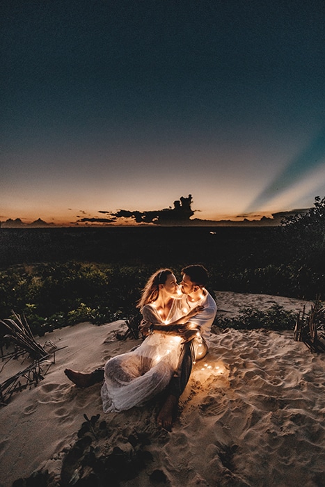 Atmosféricamente iluminado retrato al aire libre de una pareja planteada en una playa con luces de hadas