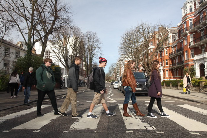 Un grupo de 5 personas cruzan la calle en Abbey Road al estilo de los Beatles