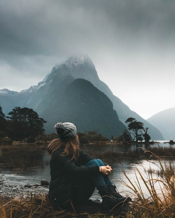 Retrato atmosférico de una modelo femenina sentada junto a un lago y un paisaje montañoso