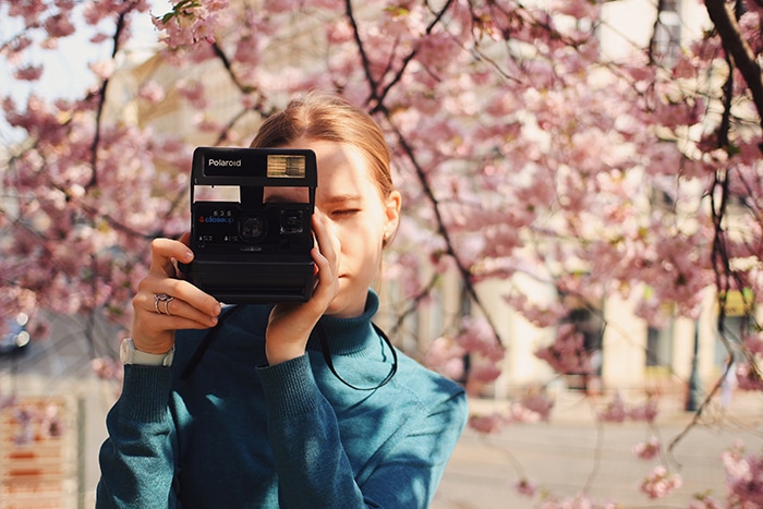 una niña tomando fotos con una cámara Polaroid debajo de los cerezos en flor