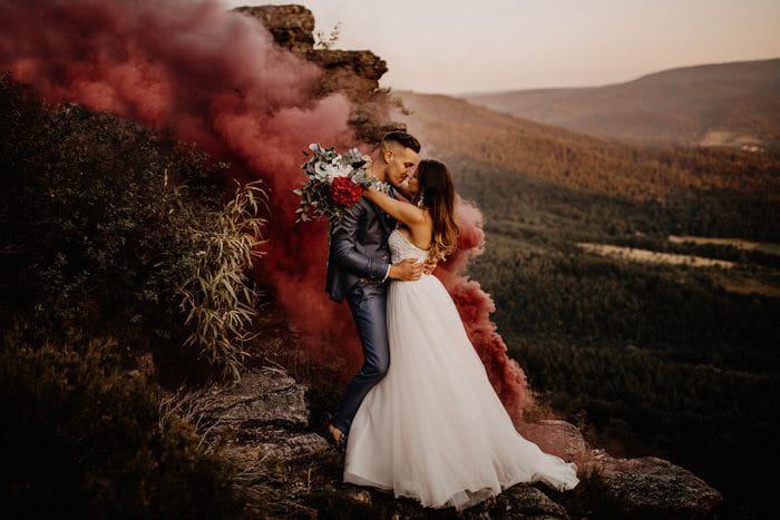 Una pareja de recién casados ​​abrazada en un paisaje atmosférico con humo detrás de ellos: los mejores blogs de bodas para seguir