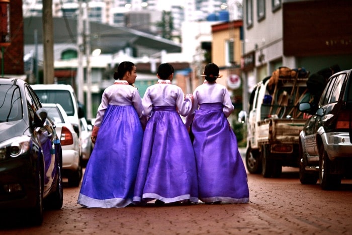 Fotografía callejera de tres mujeres con vestidos morados caminando por la calle.