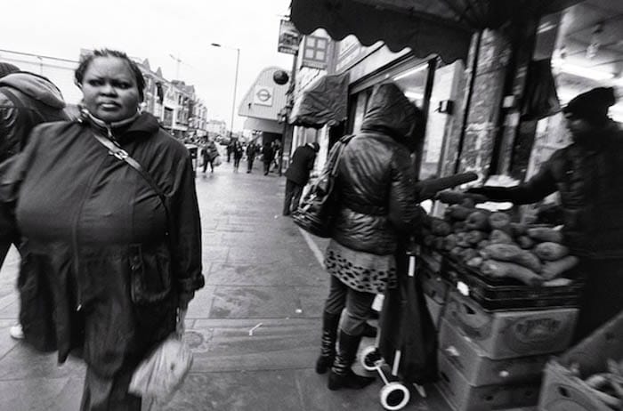 Un retrato callejero de una mujer caminando por la calle mientras otros compran verduras