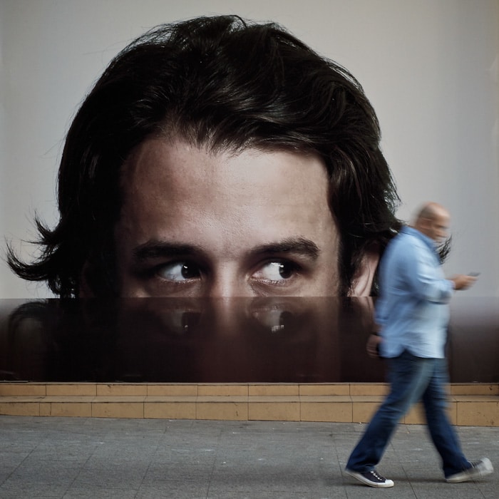 Los ojos en un anuncio parecen seguir a un hombre caminando - fotografía callejera