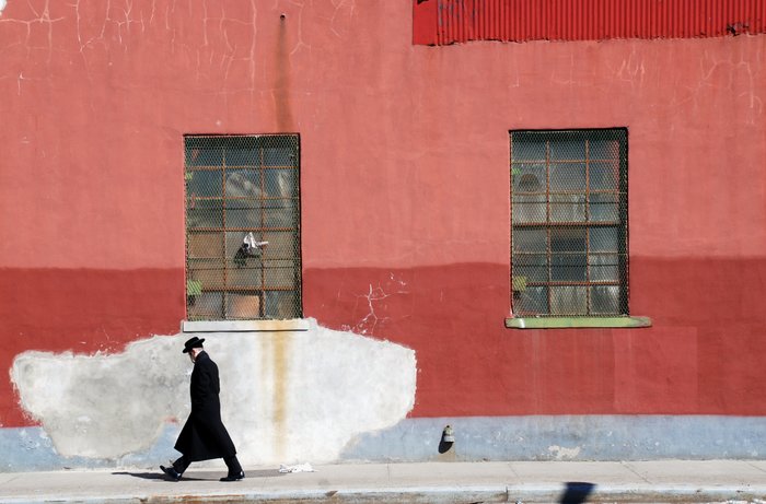 Un hombre con traje y sombrero pasa frente a una pared roja.