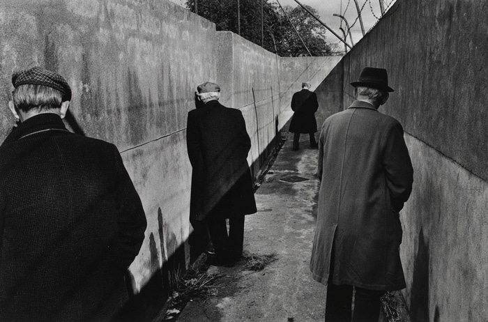 Fotografía callejera en blanco y negro de cuatro hombres parados en un pasillo sombrío orinando