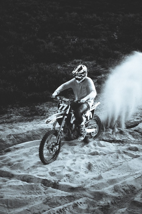 Una foto en blanco y negro de un hombre en bicicleta atravesando la arena.  Él es claramente el foco principal de la fotografía.