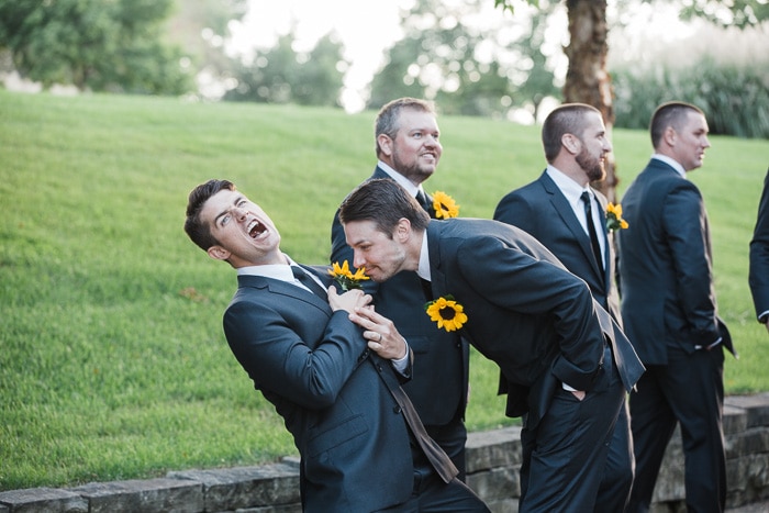 Una foto de boda chistosa que muestra a un grupo de padrinos de boda, uno oliendo el girasol en la solapa de otro hombre