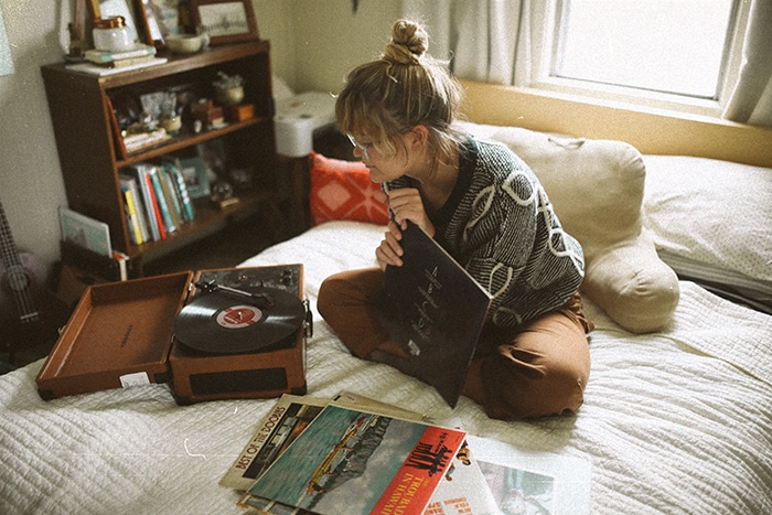 Un retrato de fotografía analógica de una niña sentada en su cama eligiendo discos de vinilo para tocar en una habitación acogedora - retratos de estilo de vida