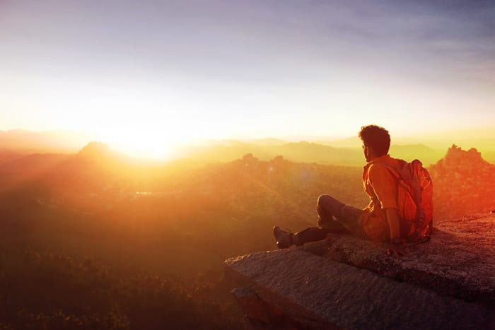 Una foto de un mochilero sentado al borde de un acantilado mirando hacia la puesta de sol.  Consejos para la fotografía con fotómetro