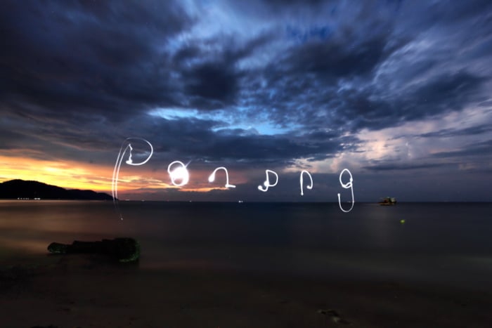 Palabras dibujadas en el cielo sobre un paisaje marino por la noche, usando la linterna de un teléfono inteligente para fotografías de pintura con luz