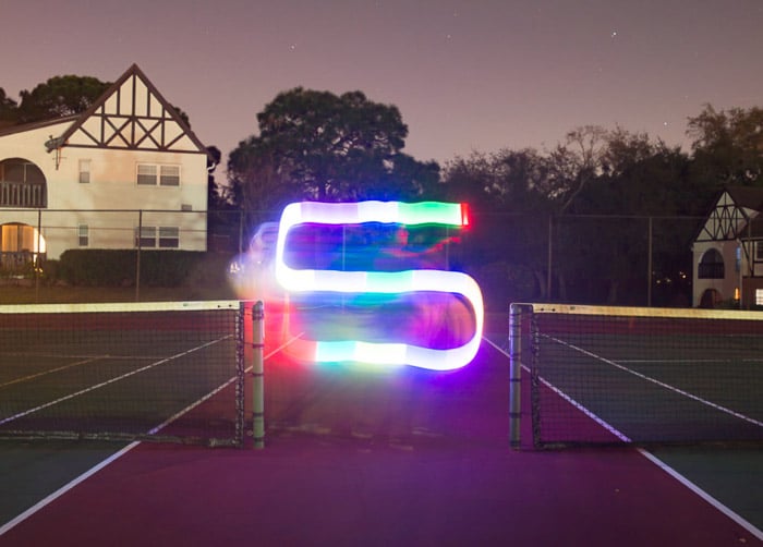 Una colorida racha de pintura con luz en forma de S filmada en una cancha de tenis por la noche usando herramientas de pintura con luz LED