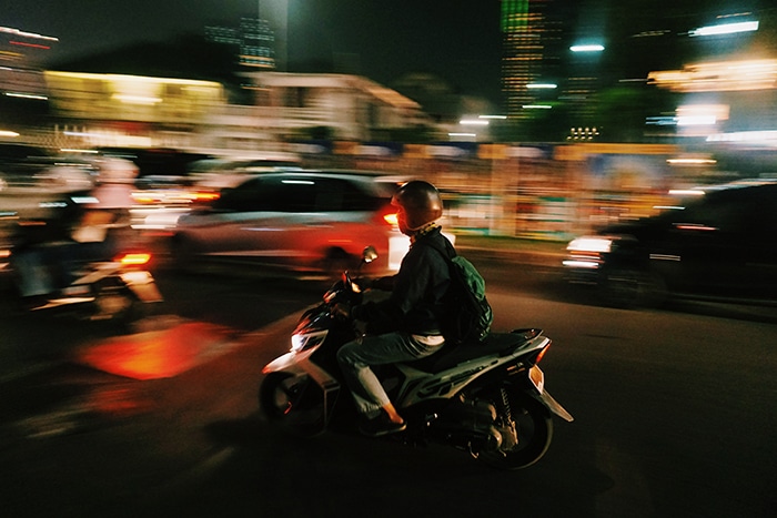 Una toma panorámica de un conductor de motocicleta con fondo borroso de tráfico en movimiento por la noche