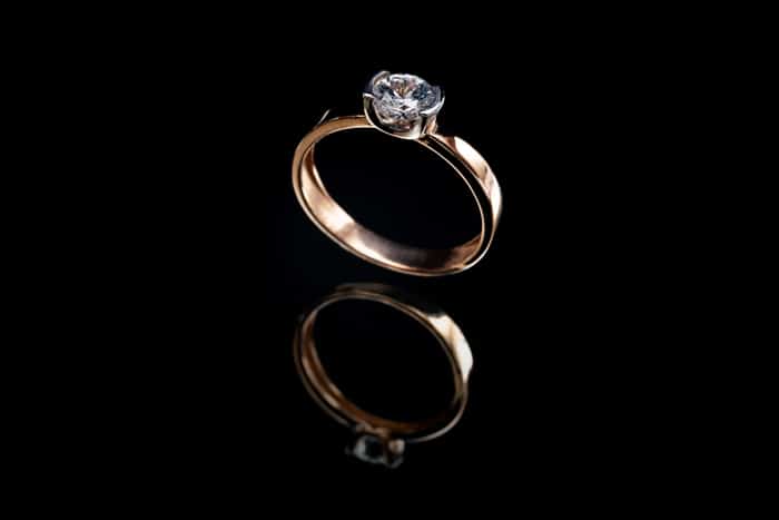 Foto de producto de joyería de un anillo de compromiso de oro sobre fondo negro y su reflejo
