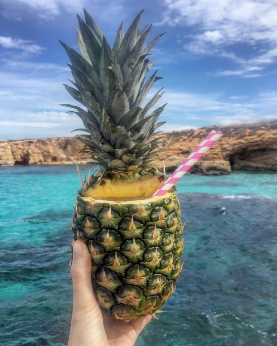 Fotografía de comida de iphone fresco de una mano sosteniendo un cóctel de piña a un paisaje marino