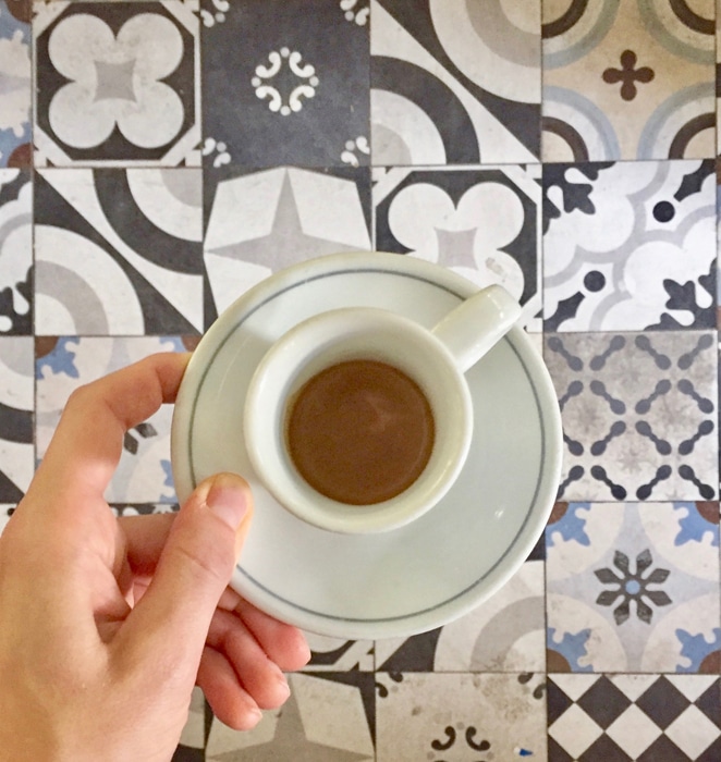 Una persona sosteniendo una taza de té sobre azulejos estampados.