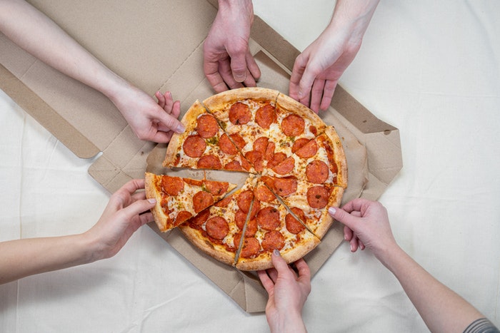 Fotografía cenital de gente agarrando porciones de pizza de una caja