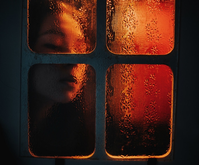 Interior atmosférico retrato de una niña empujando su rostro contra un cristal de la ventana