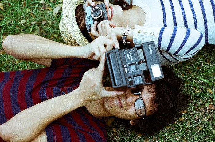 Fotografía cenital de dos personas tendidas en el césped, apuntando las cámaras al fotógrafo.  Consejos de Instagram para principiantes en fotografía.