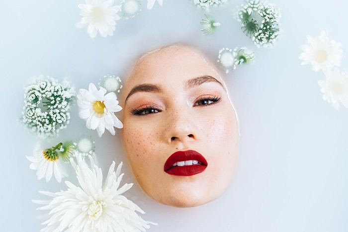 Hermosa fotografía de baño de leche de un modelo femenino rodeado de flores blancas