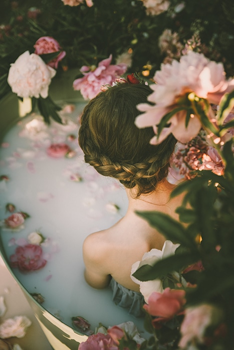 Fotografía hermosa del baño de leche de un modelo femenino rodeado de flores