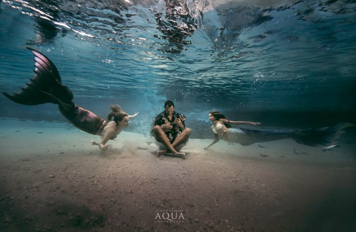 Una mágica escena de fantasía de sirena submarina con dos sirenas nadando hacia un músico submarino - consejos de fotografía de sirenas