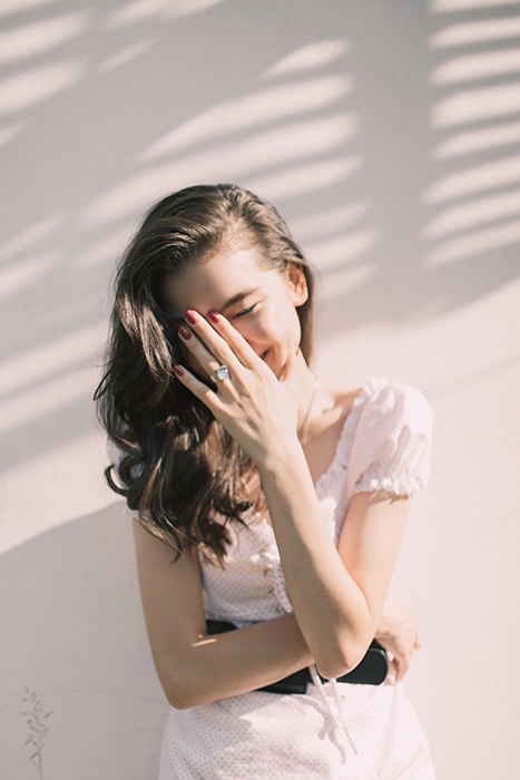 un retrato minimalista de una modelo femenina que cubre su rostro riendo con la mano