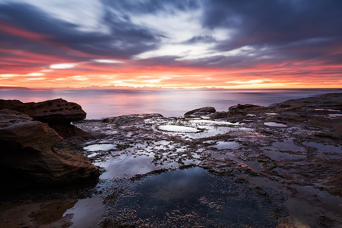 Un paisaje marino de piscina de roca dramáticamente iluminado con una puesta de sol ardiente.
