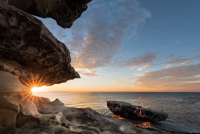 Foto de paisaje marino combinado con rayos de sol con rocas y cielo azul nublado.