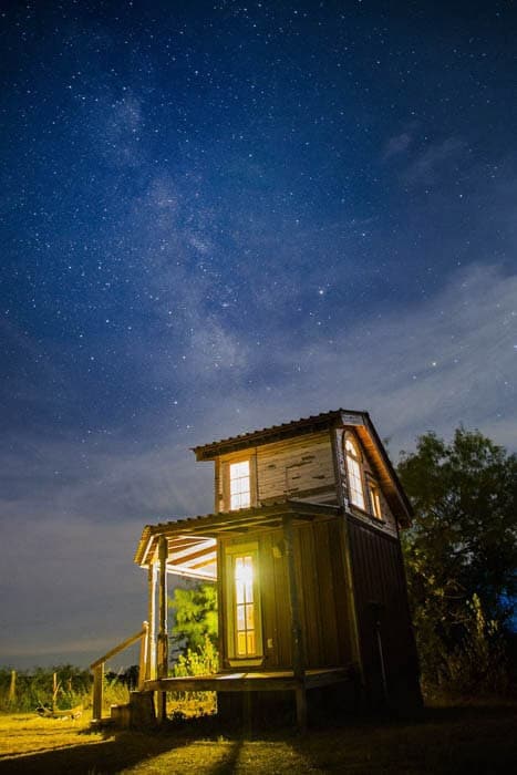 Una cabaña de madera tomada por la noche frente a un impresionante cielo lleno de estrellas.