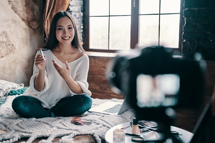 Hermosa mujer joven sosteniendo lápiz labial y sonriendo mientras fotografía fotografía de productos de estilo de vida