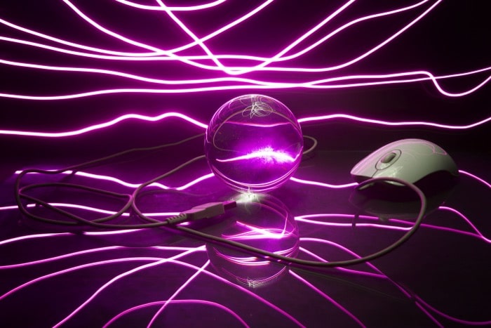 Foto atmosférica de una bola de cristal, un mouse de computadora y un cable rodeados de una impresionante fotografía de pintura de luz púrpura