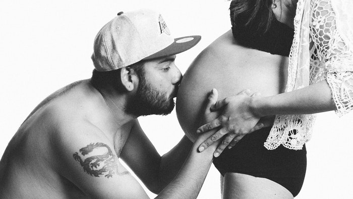 Foto de tocador de maternidad en blanco y negro de un hombre besando el vientre de su esposa embarazada